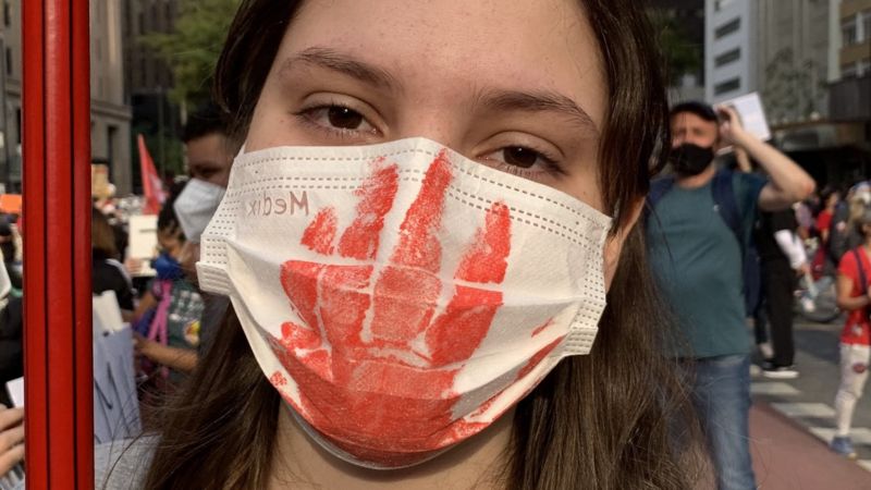 A woman wears a mask with a bloody hand print