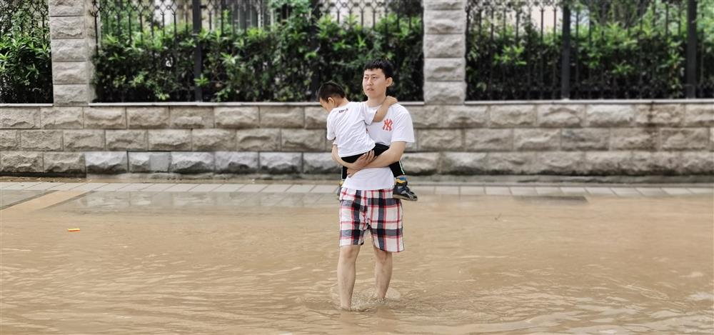 抱着孩子蹚过积水的郑州市民